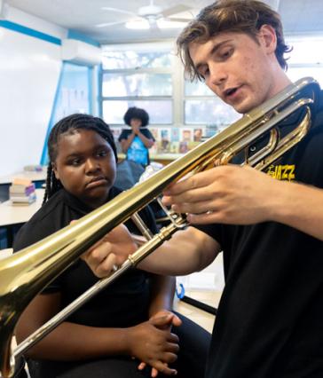 CSULB student Ben Rifkin, with trombone, interacting with a girl at a music class