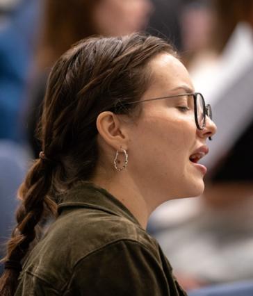 A student with glasses and a braid sings during a rehearsal.