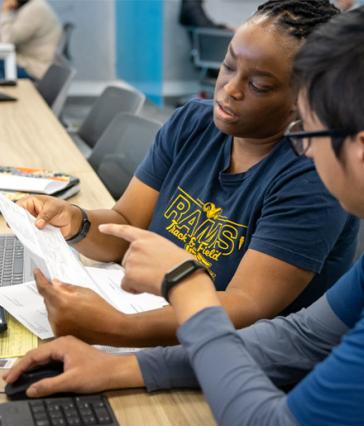 A woman in a "Rams Track & Field" shirt reviews a tax document with an accounting student at the VITA lab.