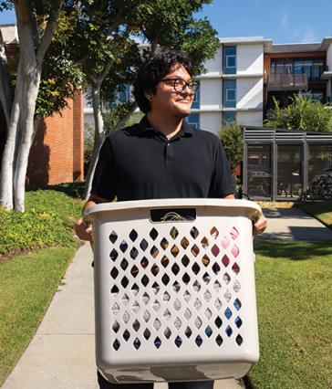 A person carries a large laundry basket outside near student housing