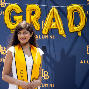 CSULB grad in front of gold GRAD balloons