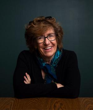 Author Barbara Kingsley-Wilson sits smiling at a table with her arms crossed in front of her.