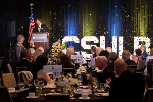 President Jane Close Conoley walking in front of a stage with a podium and "CSULB" sign during a gala