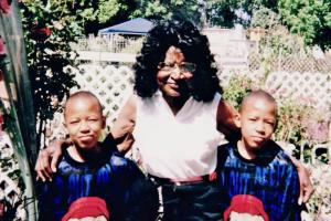 The Cooper twins in matching sports uniforms stand on either side of a relative wearing a white shirt.