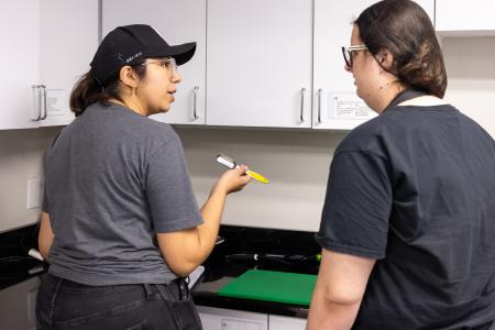 LIFE Project Coordinator Alma Jongewaard holds a kitchen utensil and talks to a Summer LIFE student in a campus kitchen.