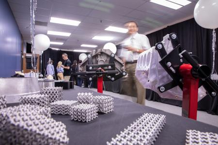 A display table showcases 3D-printed metal lattice structures and mechanical parts, while people converse in the background at the opening of the Innovation SPACE.