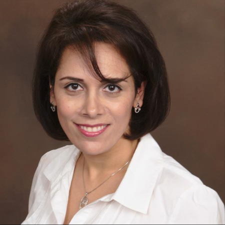 Shadnaz Asgari, a professor, smiles while wearing a white collared shirt and silver jewelry against a brown backdrop.