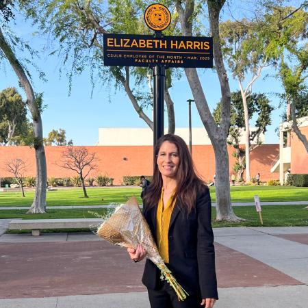 Employee of the Month Elizabeth Harris A woman holds flowers and stand in front of a sign that says "Elizabeth Harris"