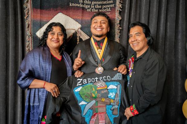 Native American graduate in cap and gown with parents.