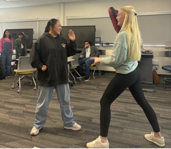 During a self-defense seminar by University Police, Beach XP student Sammi Nakahara (left) learns from campus Emergency Manager Allyson Joy how to set up a defense pose and strike a possible threat.