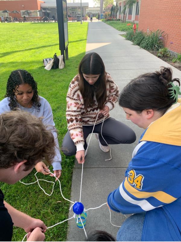 CSULB Student Life & Development leads an activity in which Beach XP students pull on strings to carry a ball over to and into a cup without dropping it. It’s designed to build communication and collaboration skills.