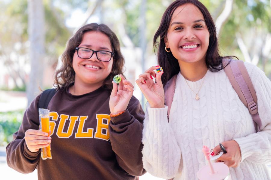 Two students smile at camera while holding decorative pins