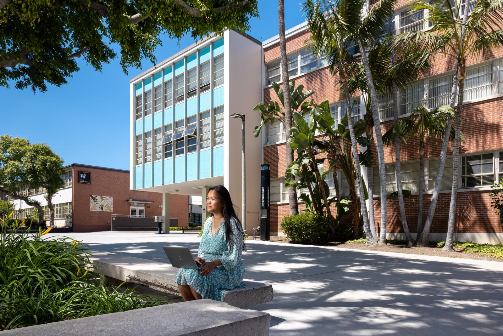 A person sits on bench and uses a laptop.