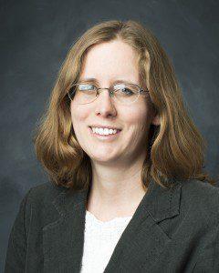 Smiling white woman with medium length light brown wavy hair wearing glasses, a white blouse and black jacket