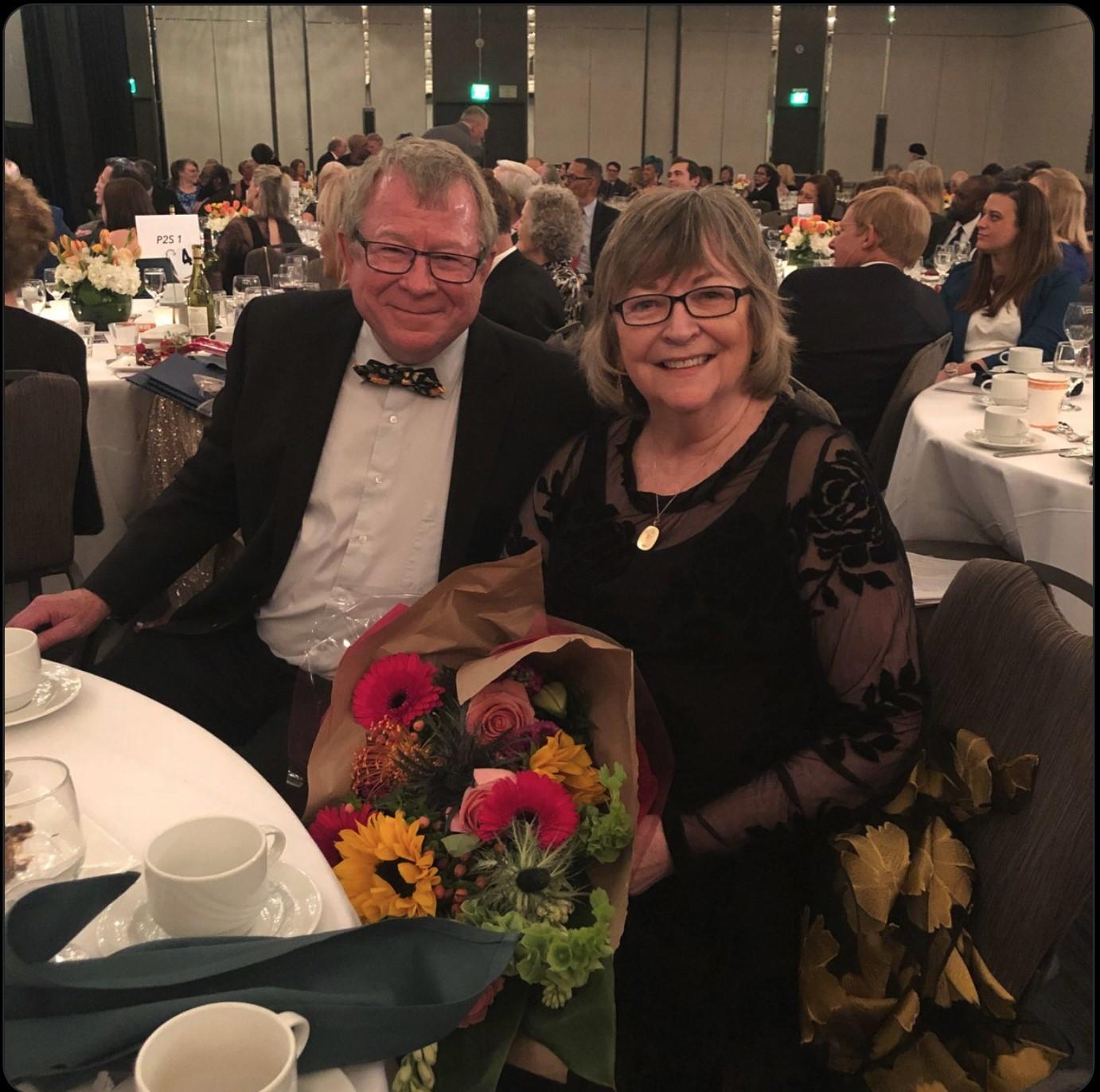 President Jane Close Conoley seated next to her husband while holding a bouquet