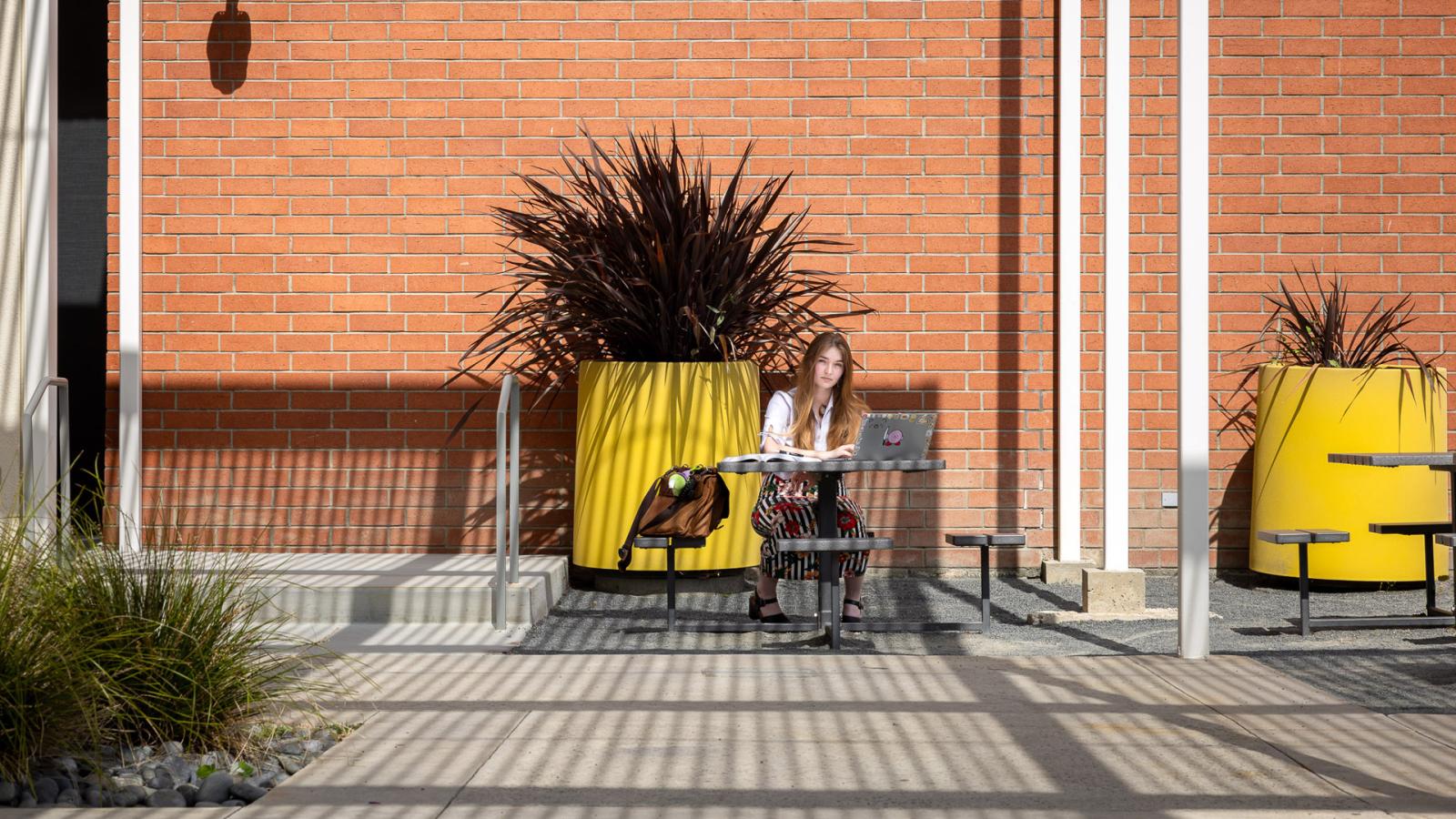 Katrina Watson sits at a picnic table with her laptop in front of a brick building