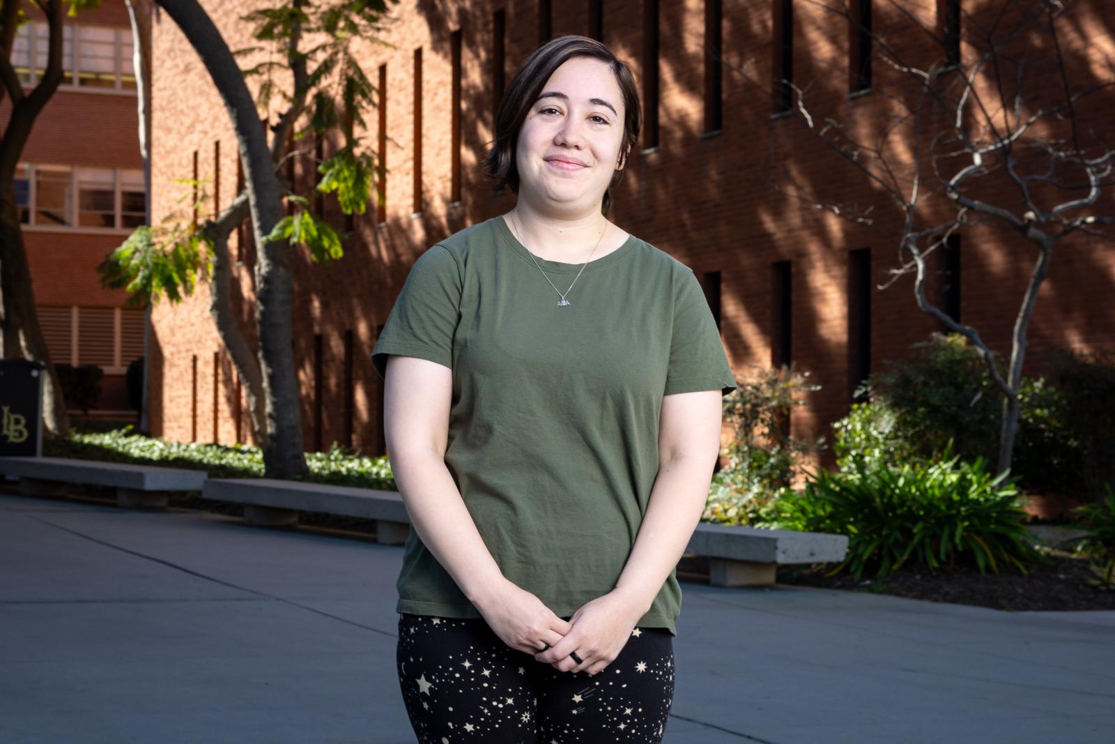 Teaching student Marisa Saxon stands in front of a brick building with trees and benches in the background