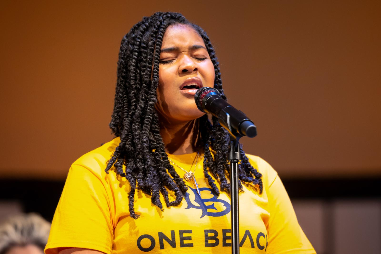 A student in a "One Beach" shirt sings into a microphone at the Community Gospel Choir Concert