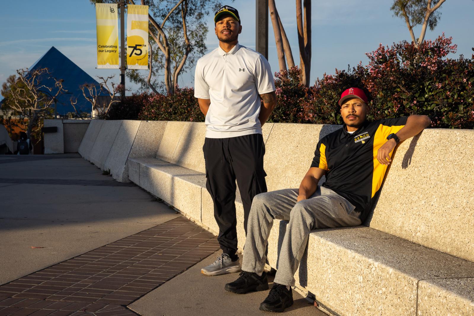 Martel and Markel Cooper sit on campus with the Pyramid and 75th anniversary banner behind them.